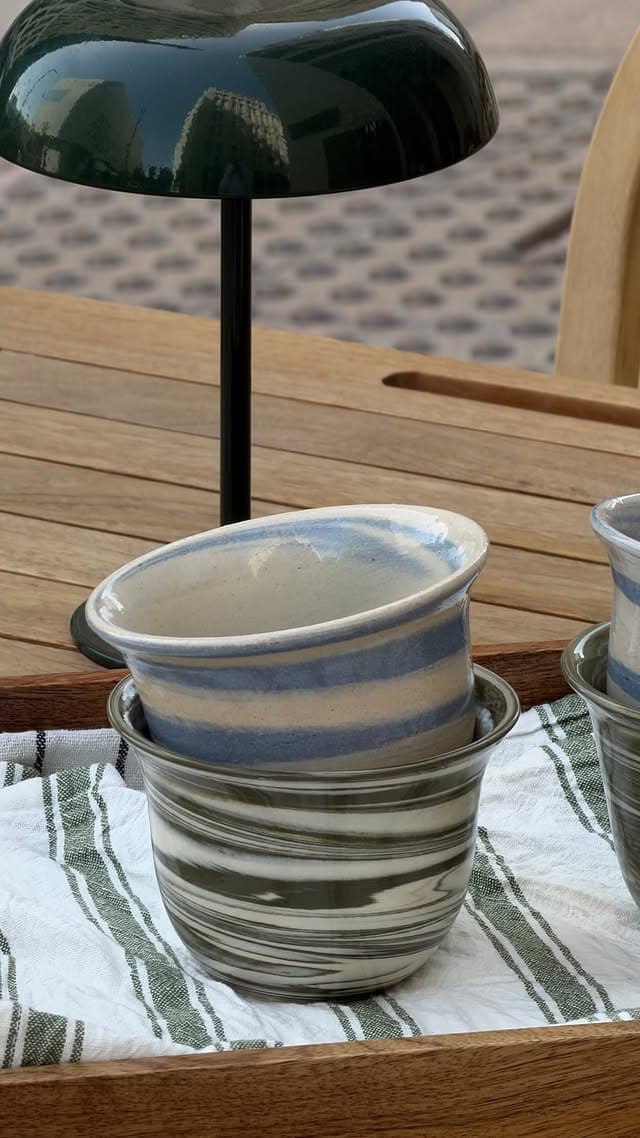 Close view of two stacked funjans, blue-and-cream above olive-and-cream, under a green dome lamp.