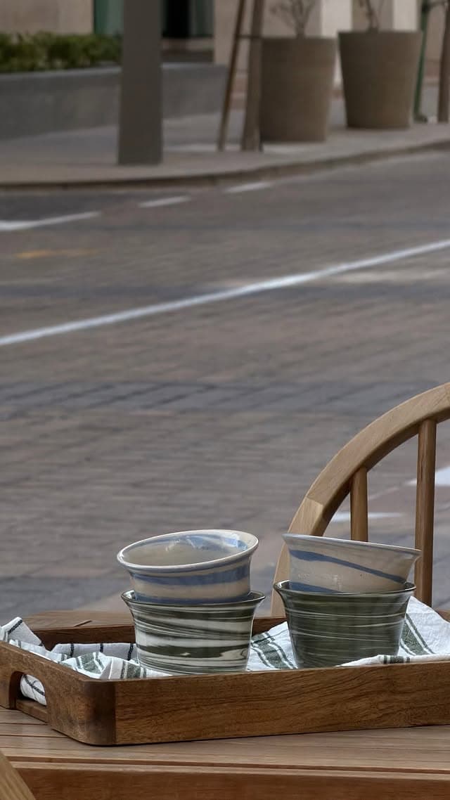 Ceramic funjans on a wooden tray on the café terrace, with the pavement, a low wall and planters across the street behind.